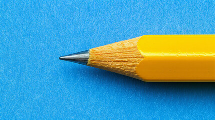 A yellow pencil with a sharpened point is on a blue background. The pencil is the main focus of the image, and it is a simple, everyday object. The blue background adds a sense of calmness