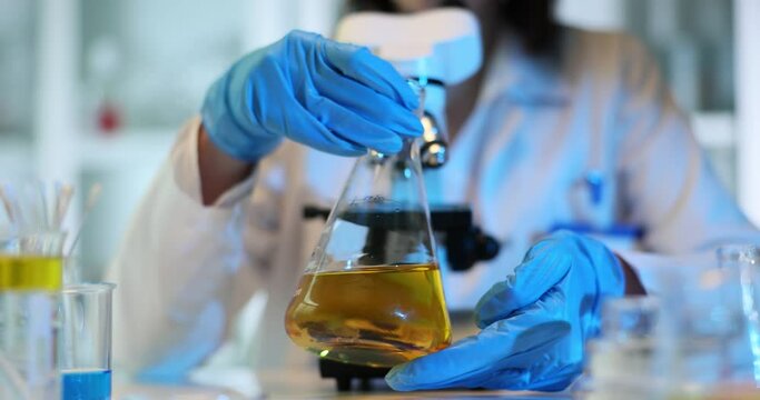 Scientist holds and tilts flask with a yellow liquid