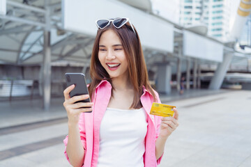 Happy Asian girl standing using smartphone and holding credit card with enjoys freedom.