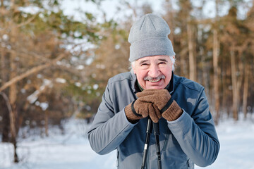 Portrait of cheerful senior Caucasian man standing outdoors on winter day posing for camera with...