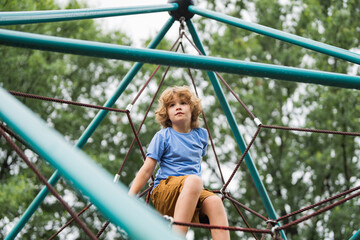 Kid play on playground under the tree. Portrait of cute blonde kid doing rock climbing with greenery in the background.