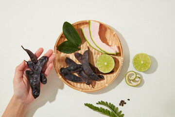 A beautiful hand is holding some black locust, a rattan tray with ingredients for produce manufacturing of haircare. Photo for advertising or branding
