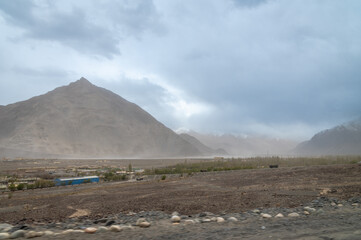 Rocky Terrains of Nubra Valley in Ladakh, India. Background of Himalayas and dramatic clouds. View of cars driving through the zig zag Himalayan roads.