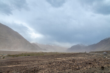 Rocky Terrains of Nubra Valley in Ladakh, India. Background of Himalayas and dramatic clouds. View of cars driving through the zig zag Himalayan roads.