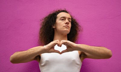 Studio shot of a gay man doing heart symbol shape with hands isolated on purple background