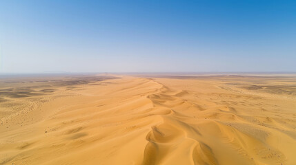 Aerial view of a vast desert with sand dunes rippling towards the horizon under a clear blue sky