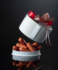 Opened gift box with sausages on a black background.
