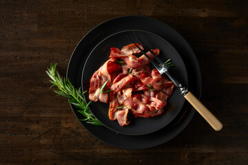  Roasted bacon slices with rosemary on an  old wooden table.