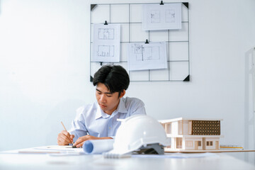 Closeup portrait image of architect engineer writing, drawing, taking a note about house model...