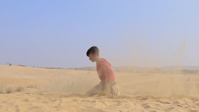 boy playing with yellow sand at desert at day video is taken at rajasthan, India.