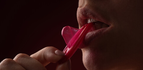 Mouth of sensual girl with condom. Protection, safe sex and Contraceptive concept. Condom in the mouth of women, close up. Open mouth and sexy lips, lick condom. Condom in mouth of sexy women. - obrazy, fototapety, plakaty