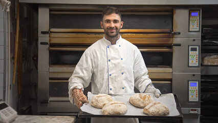 Handsome baker show done bread loafs bakery shop. Smiling man bake buns portrait