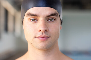 Caucasian boy with brown hair, green eyes in black cap stands indoors near water