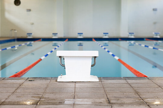 Swimmers are not visible indoors, only an empty starting block by the poolside