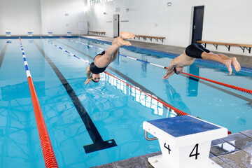 Diverse young swimmer competitors, friends diving into an indoor pool, training together