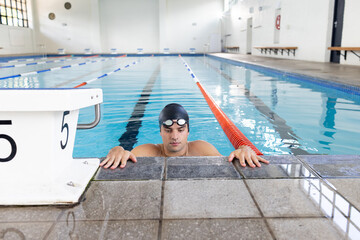 Caucasian young male swimmer wearing cap and goggles, resting at swimming pool edge
