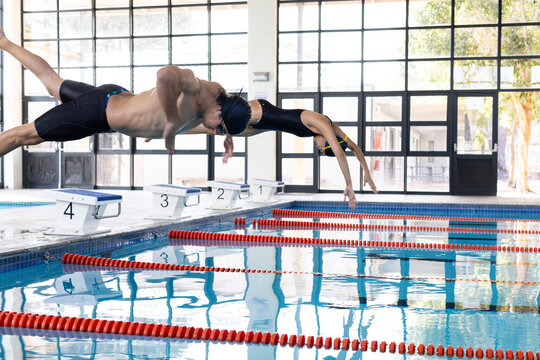 Diverse young swimmer competitors, including a Caucasian male and biracial female, diving into a poo