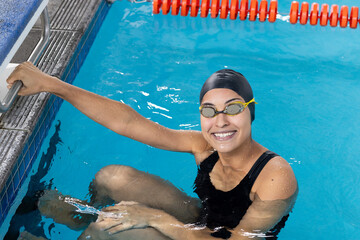 Biracial girl in goggles grips indoor pool edge