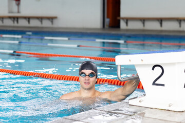 Caucasian young male swimmer resting at swimming pool edge, wearing goggles