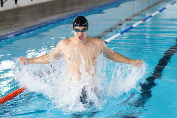 Caucasian young male swimmer training indoors in swimming pool, making a splash