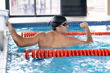 Caucasian young male swimmer with dark hair is training indoors in a pool