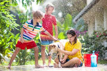 Kids wash dog in summer garden. Water hose fun.