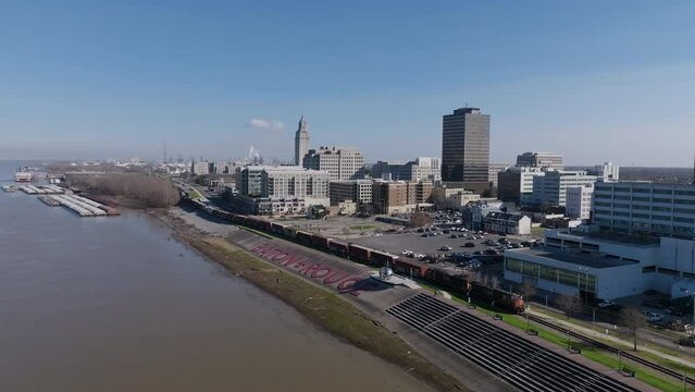 Wide aerial footage of the Baton Rouge sign on the banks of the Mississippi River with downtown in the background and a train moving by the sign.