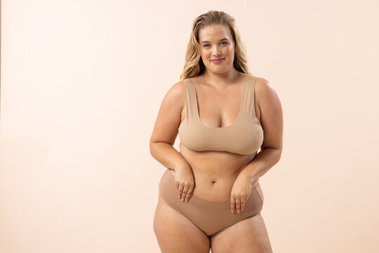 A young Caucasian plus-size model poses on beige background, copy space