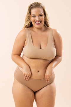 Caucasian plus-size model in beige underwear stands and smiles