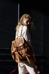 Naklejka premium beautiful curly blond hair woman posing with a leather backpack