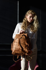 beautiful curly blond hair woman posing with a leather backpack