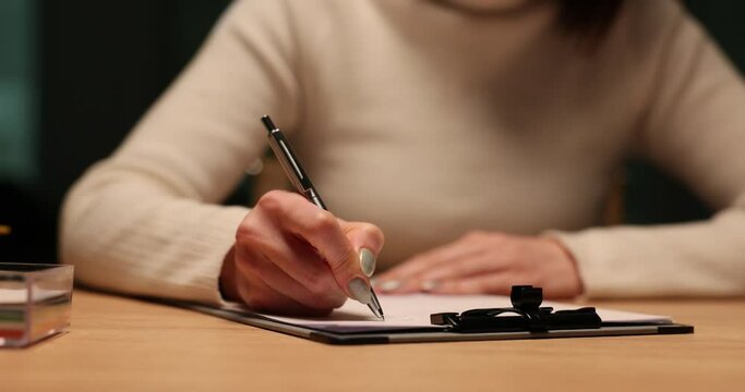 Woman signs a document at table in evening in office
