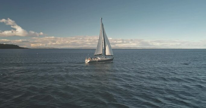 Slow motion of racing yacht at open sea aerial. Passengers on cruise sail boat. Serene seascape of Brodick Gulf, Arran island, Scotland, Europe. Luxury sailboat at ocean bay. Cinematic summer vacation
