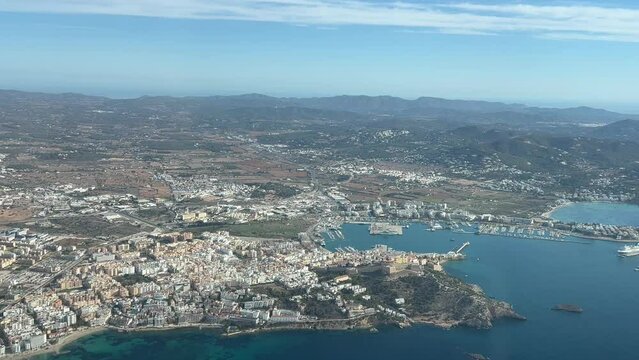 Aerial view of Ibiza city, Spain, shot from a plane cockpit departing from the airport. Left window side. Sunny day, blue sky. 4K