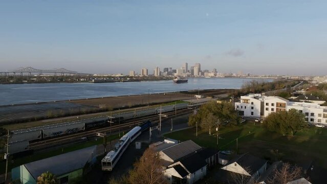 Aerial flyover of a passenger train moving towards downtown with a large container ship on the Mississippi River with downtown New Orleans in the background in the morning.