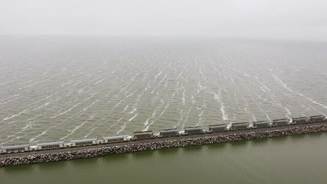 Wide aerial pan of long freight train on straight track by sea in Argentina