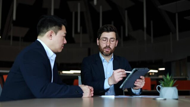 Intelligent caucasian male in business suit using tablet computer for simplification of communication with partner. Contemporary team leader presenting simulation of company indicators growth.