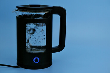 Water boiling in black electric kettle on blue background. Copy space for text.