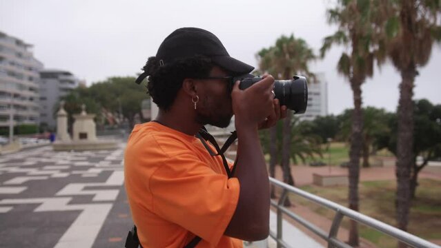 South African man in orange t-shirt takes photos with camera near palm trees in Cape Town, South Africa