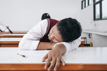 Tired student sleeping at desk in classroom during lesson