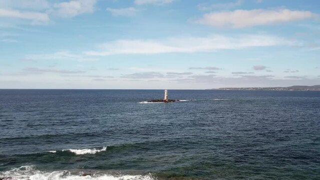 Drone footage of Faro di Mangiabarche in the middle of the sea on a sunny day with blue sky in Italy