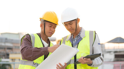 Structural engineer and architect working with blueprints discuss at the outdoors construction site.