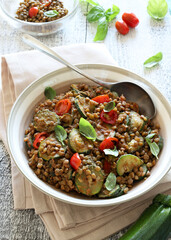 Lenticchie con zucchine e pomodorini aromatizzate con foglie di basilico. Contorno o secondo piatto su sfondo bianco. Cibo vegano. Direttamente sopra.