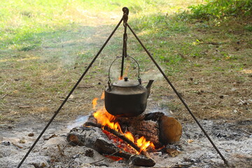 A smoked aluminum kettle hangs on a tripod over a fire.