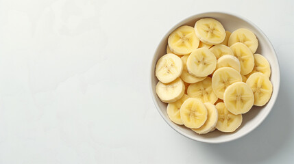 A vibrant bowl of banana slices on a pristine white table, offering a healthy and delicious snack with a clean, minimalist appeal.