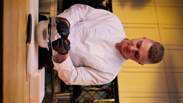 vertical video assistant chef in the kitchen in white jacket cuts beets in his hands over the table
