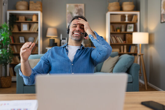 Excited biracial male call center agent in headset have fun laugh working on computer online, overjoyed man busy studying or watching funny training webinar on computer gadget