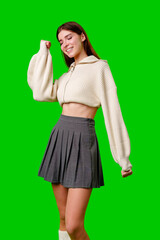 A smiling young woman strikes a playful pose, wearing a white crop-top sweater and a gray pleated skirt.