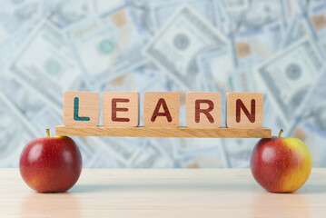  Image symbolizing the value of education, with LEARN spelled out on wooden blocks perched on apples, set against a backdrop of assorted currency notes