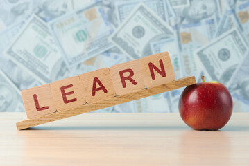 A conceptual image of investing in education, featuring LEARN spelled out on wooden blocks balanced on apples, with a background of various currency notes